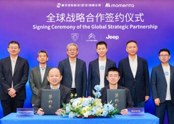 Momenta and DSAT representatives hold agreement folders at a global strategic partnership signing ceremony, with executives standing behind them.